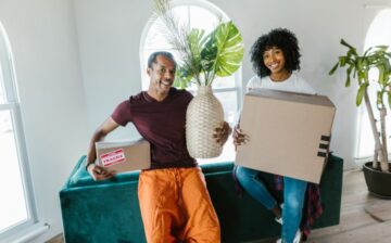 a couple holding a moving box and a vase with plant