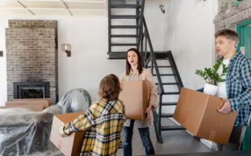 a mother, father and son each are holding a packed moving box